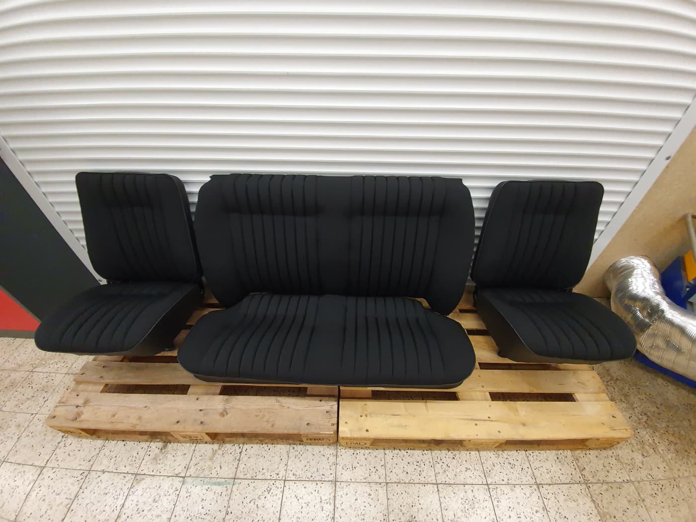 Drei schwarze Sitze auf Palette, andere Ansicht