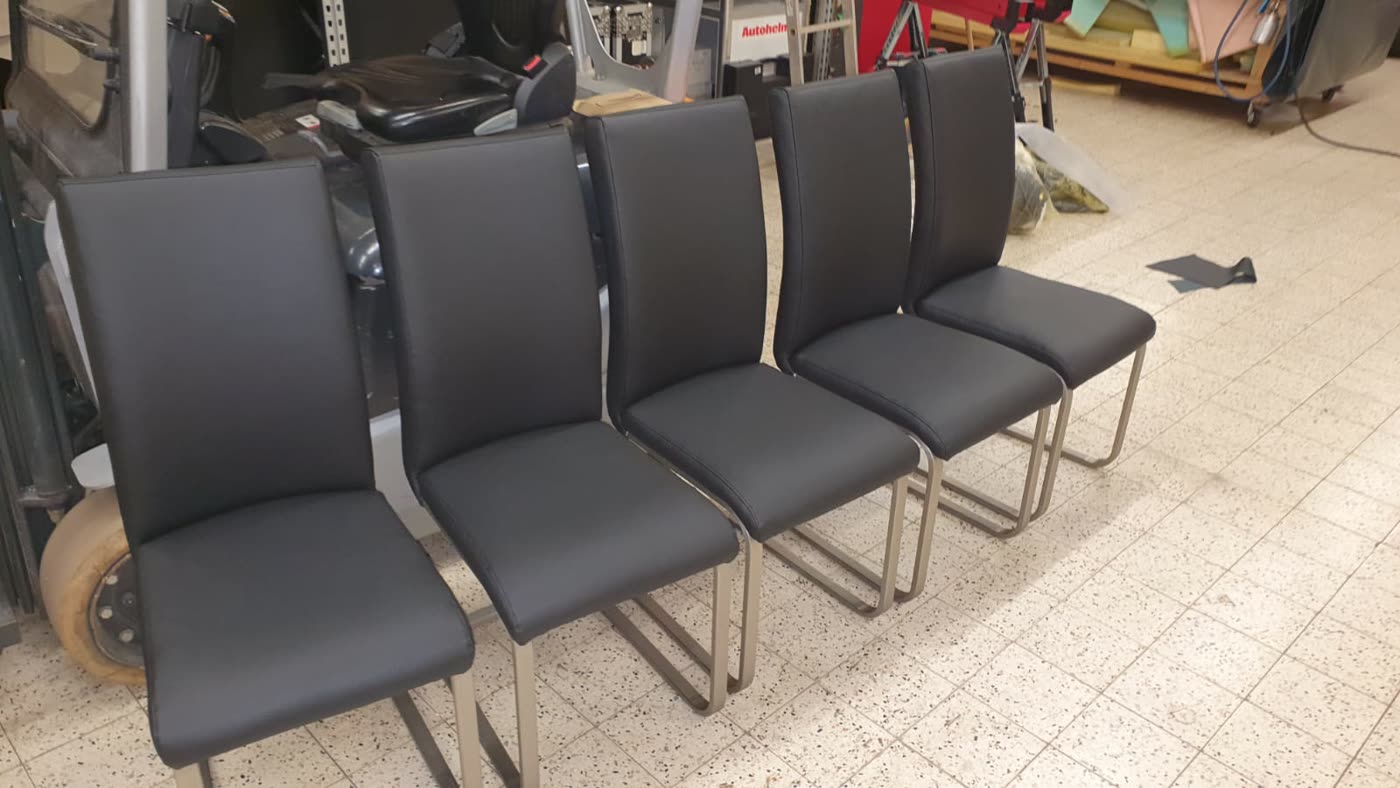 Fünf schwarze Stühle mit Chromgestell, unruhiger Werkstatt-Hintergrund