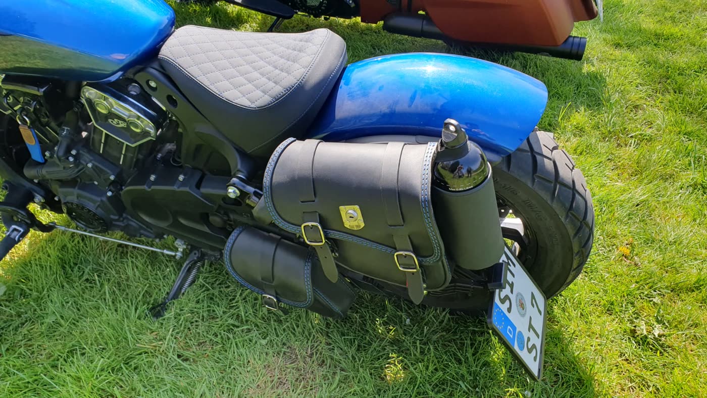 Blaues Motorrad mit Ledertasche und Sitzbank, im Gras